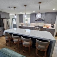 A luxurious kitchen with gray cabinets, a large island with pendant lighting, and high-end appliances.
