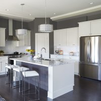 A modern kitchen with gray walls, white cabinets, and stainless steel appliances. The kitchen has a large island with seating and a chandelier overhead.