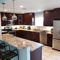 A spacious kitchen with dark wood cabinets, granite countertops, and stainless steel appliances. The room has pendant lights and an island with bar stools.