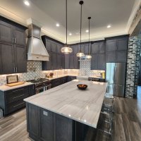 A modern kitchen with dark gray cabinets, white countertops, and pendant lighting fixtures.