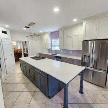 The image shows a modern kitchen interior with white cabinets, stainless steel appliances, and a large island with a white countertop.