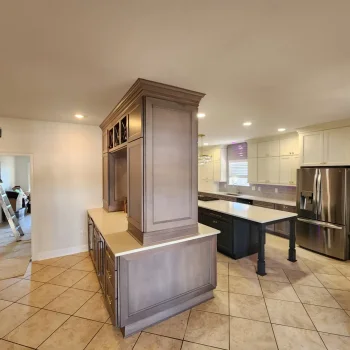 Peninsula Kitchen Cabinetry, light brown cabinetry with gold hardware and white quartz countertops wine cooler and ice maker. Wine racks with wine bottles in them side shot