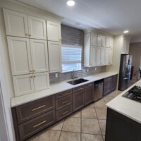 White painted upper kitchen cabinets with light gray stained lower base kitchen cabinets with gold handles hardware