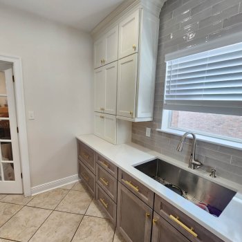 White painted upper kitchen cabinets with light gray stained lower base kitchen cabinets with gold handles hardware and stainless steel undercounter kitchen sink