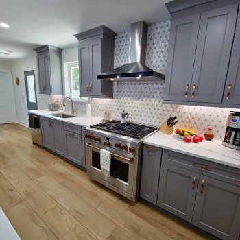 Blue gray kitchen cabinetry with white quartz countertops that has dark veining, cabinetry has gold hardware tile backsplash has a sunburst pattern.