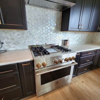 Black kitchen bar cabinetry with gold hardware handles and Michelangelo vicostone quartz countertops, backsplash is hexagonal marble tiles and Viking stove range and vent hood