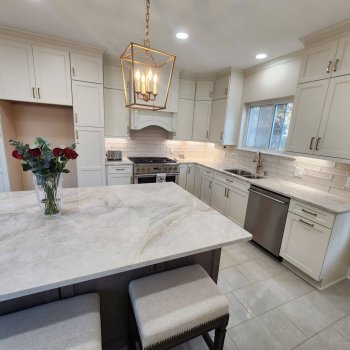 Off white kitchen cabinetry cabinets with dark stained island, countertops in taj mahal quartzite and gold handles hardware, Viking range stove and wood hood gourmet style, 8 inch subway tile backsplash