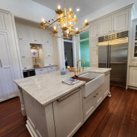 A spacious kitchen with white cabinetry, a marble-topped island, and a large brass light fixture.