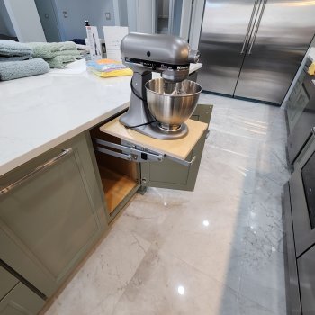 The image shows a kitchen with a large stainless steel refrigerator, a silver stand mixer on the counter, and a marble countertop with a built-in cabinet below it.