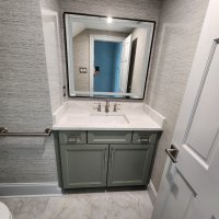 The image shows a bathroom vanity with a gray cabinet, a white marble countertop, and a large rectangular mirror mounted on the wall. The walls are covered in a gray textured wallpaper.