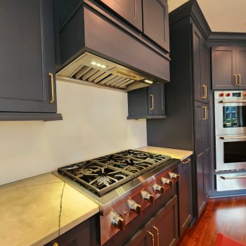 A kitchen with dark blue cabinets, a stainless steel range hood, and a marble-like countertop