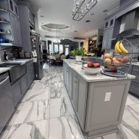 A spacious, modern kitchen with grey cabinetry, marble countertops, and stainless steel appliances. The kitchen has an island and a large window, creating a bright and inviting atmosphere.