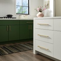 A modern kitchen interior with green cabinets, white countertops, and gold hardware