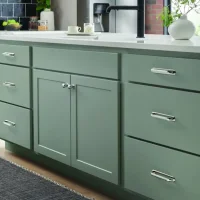 A kitchen interior with dark gray cabinets and gold hardware, displaying the 'Top Knobs' logo