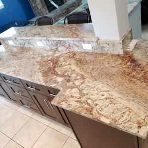 Belle Chasse granite countertops bring unrivaled depth and warmth to this home in Plaquemines Parish. This shot displays a massive, multi-level kitchen island topped with Sienna Bordeaux granite. The stone's intricate blend of deep reds, rich creams, and brown veining perfectly complements the solid cherry wood cabinetry below. Belle Chasse granite countertops featuring a two-level island in Sienna Bordeaux granite over cherry cabinetry in Plaquemines Parish.