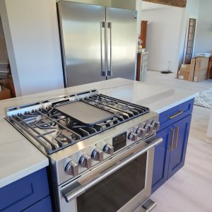 Professional chef setups paired with premium Luling quartzite countertops. This cooking zone perspective shows the immense amount of durable prep space flanking both sides of the integrated stove surface, showcasing why natural quartzite is the ultimate material choice for high-heat kitchen zones. Front perspective of a Mont Blanc Quartzite kitchen island highlighting the integrated stainless steel cooking surface and flanking stone prep space in Luling, LA.