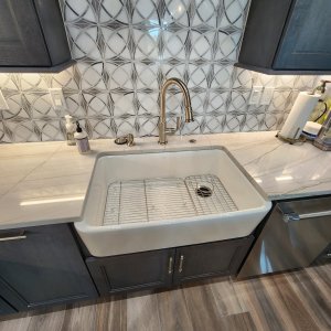 Flawless finishing on our custom Mandeville quartzite countertops. This final close-up showcases a porcelain farm-style sink seamlessly wrapped by 3cm Sea Pearl Quartzite along the front, back, and sides, creating an integrated, water-impervious wash station built to handle daily use beautifully. Close-up of an undermount white porcelain farm-style sink wrapped in 3cm Sea Pearl Quartzite countertops by French Quarter Facades in Mandeville, LA.