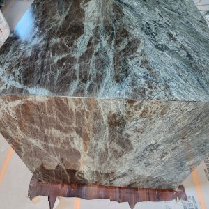 True stone artistry. Our local New Orleans quartzite countertop fabrication stands out in this close-up view, highlighting how the natural green and emerald veining cascades flawlessly over the mitered edge. This durable, luxury natural stone brings a highly unique, artistic focal point to the kitchen layout. Close-up of a Verde Esmeralda Quartzite waterfall island with a seamless 45-degree mitered edge installed in Orleans Parish by French Quarter Facades.